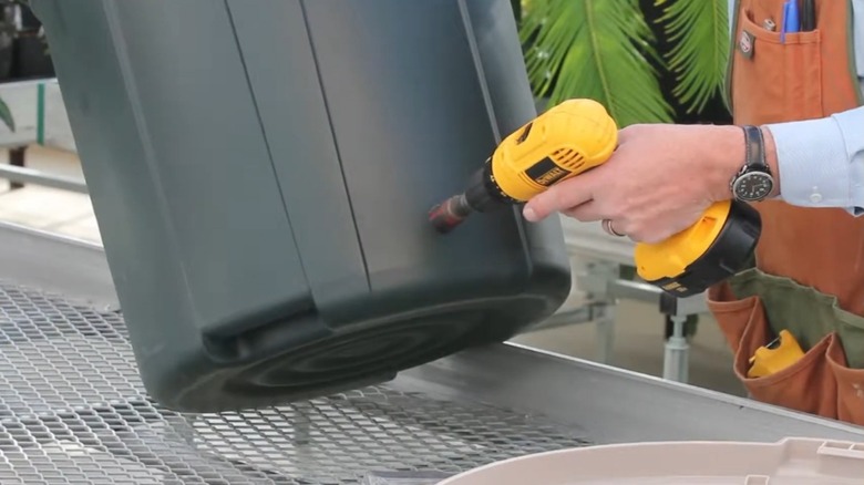 Person drilling hole into a trash can.