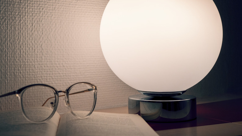Glasses and book resting beside a glowing sphere lamp like IKEA's FADO lamp.