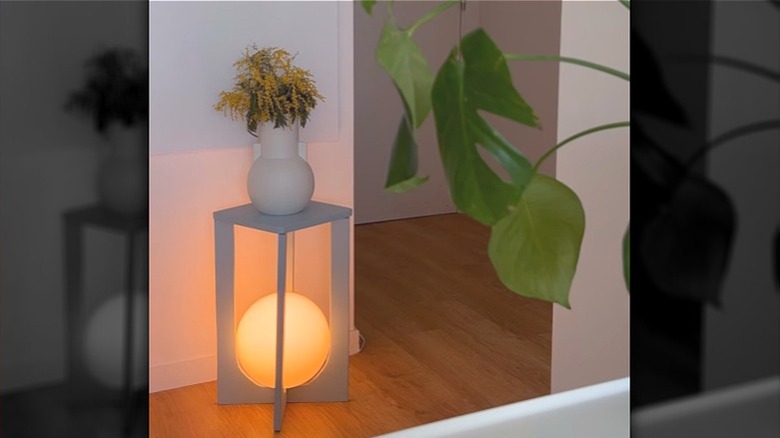 A DIY nightstand with a FADO lamp from IKEA built into the base and a vase of flowers on top.