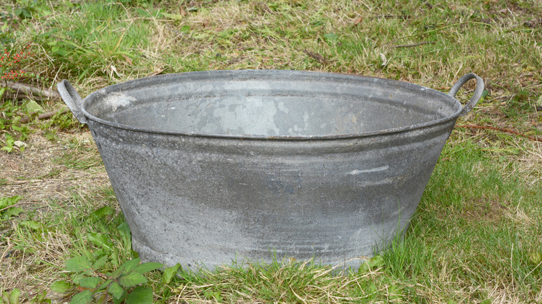 A gray antique wash bin sitting on some grass