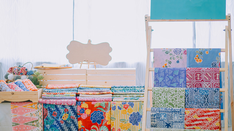A quilt rack displaying many types of colorful fabrics next to a shelf with more fabrics on it