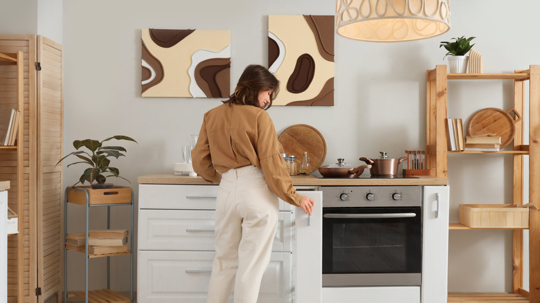 Person standing in modern kitchen surrounded by wooden baskets, trays, and copper cookware