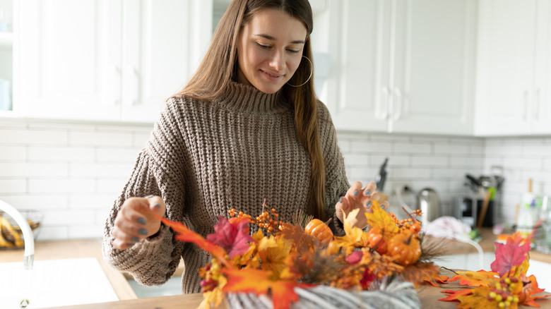 A person arranging a fall-themed wreath in her kitchen