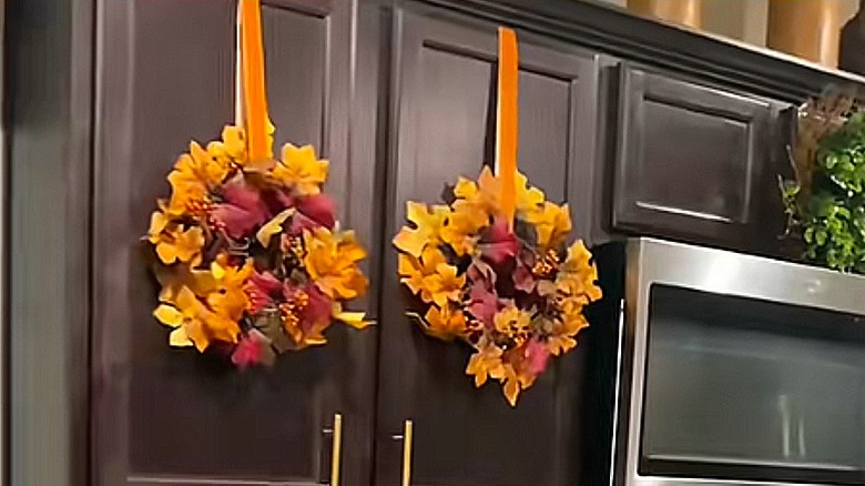 Two fall wreaths hung on the outside of kitchen cabinets with ribbons