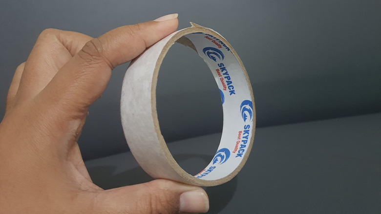 A person holds an empty tape roll in one hand.