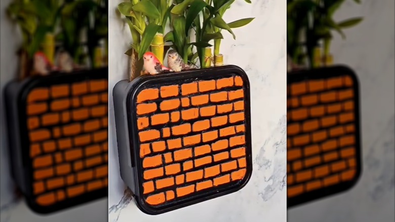 DIY wall planter made from an ice cream tub with a brick pattern on front and plants coming out of the top