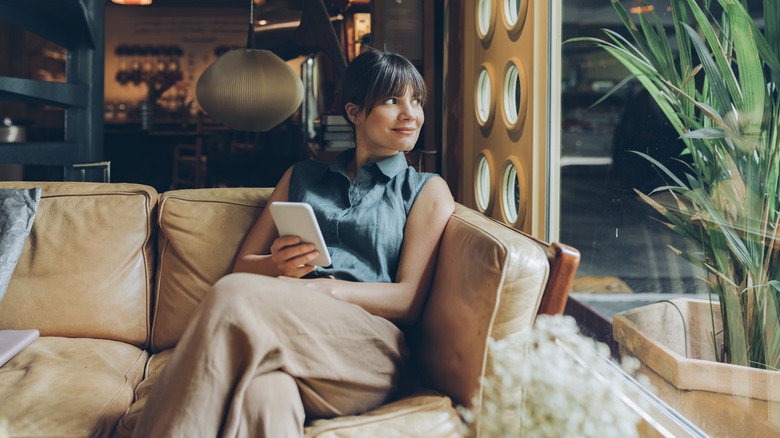 A woman sits on a couch near a window in modern cafe.