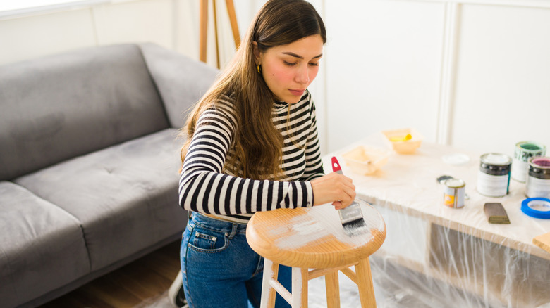 Person painting wooden stool white in front of couch