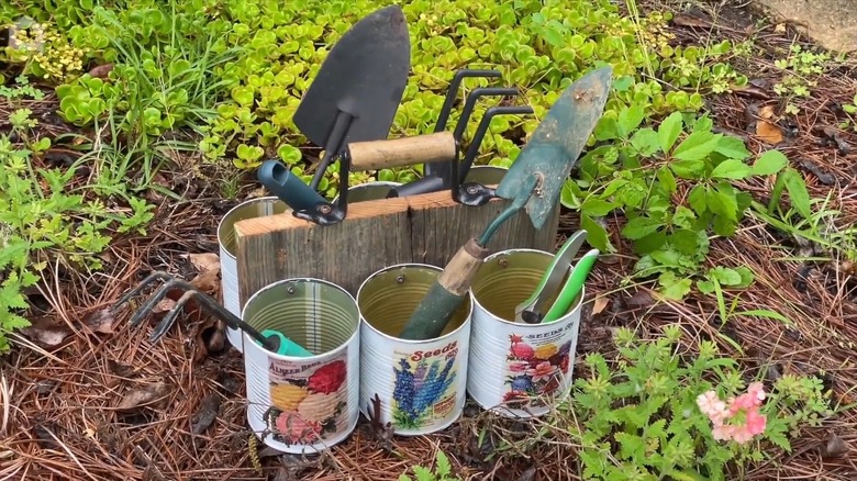 DIY garden caddy with aluminum cans holding gardening tools.