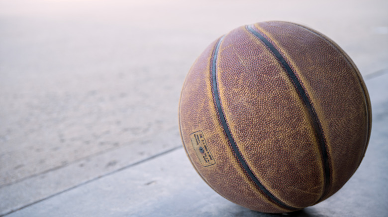 An old basketball sitting on a driveway.