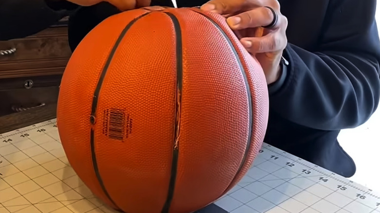 Man's hands using a precision craft knife to cut into a basketball along the black lines