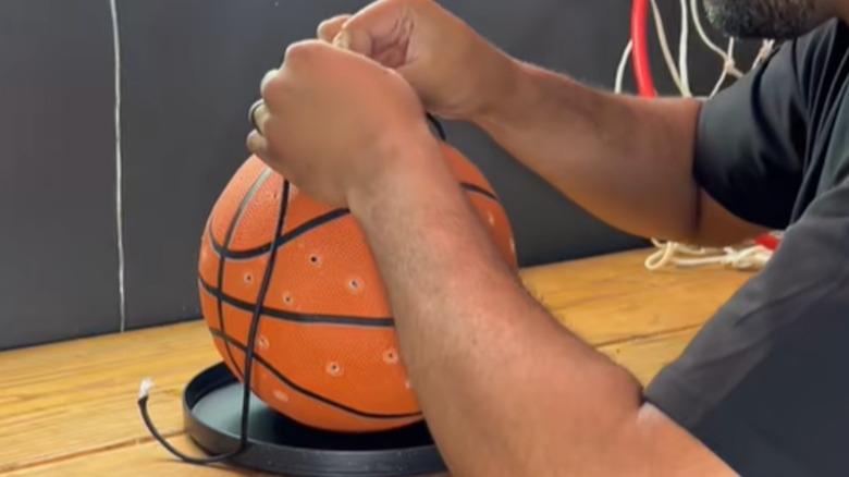 An man ties hanging cords to a basketball bird feeder with holes drilled around its circumference