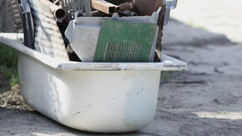 An old bathtub sitting outdoors and filled with other bits of scrap.