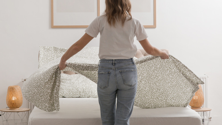 Women laying out bedsheet across a bed.