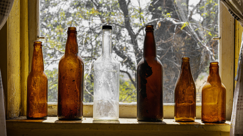 A collection of old brown and white glass beer bottles arranged on a sunny windowsill.