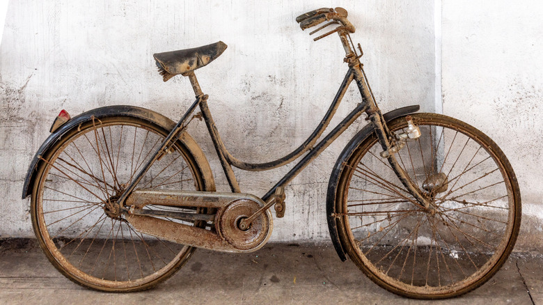 A very rusty, neglected bike leans against a white exterior wall.