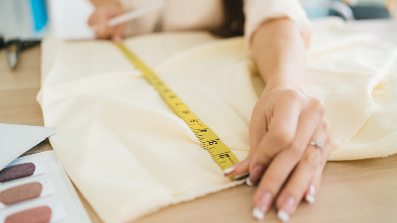 A person measures a piece of white fabric on a wooden table