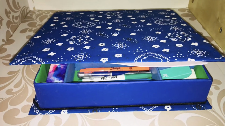A finished binder-turned-desk storage covered with dark blue bandana fabric holds pens, erasers, and more.