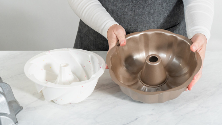Woman holding a bundt pan on a counter with two other bundt pans of different colors and shapes.