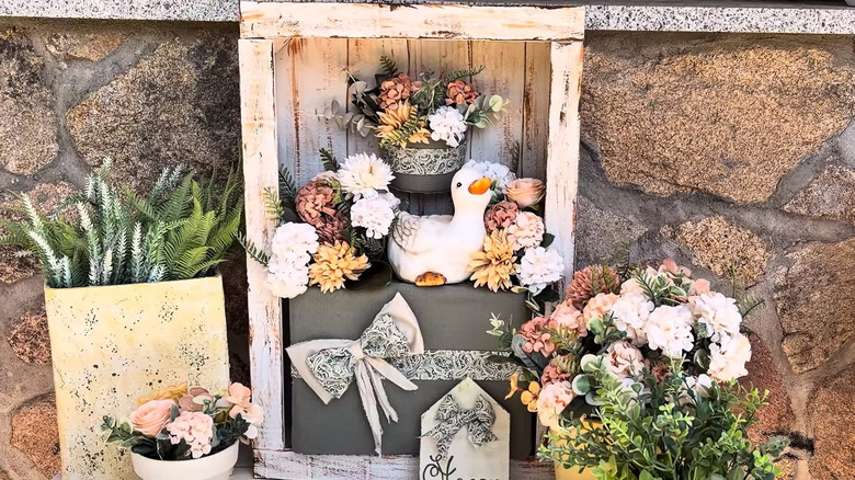 A screenshot from a video showing the shadow box and several planters with faux flowers inside