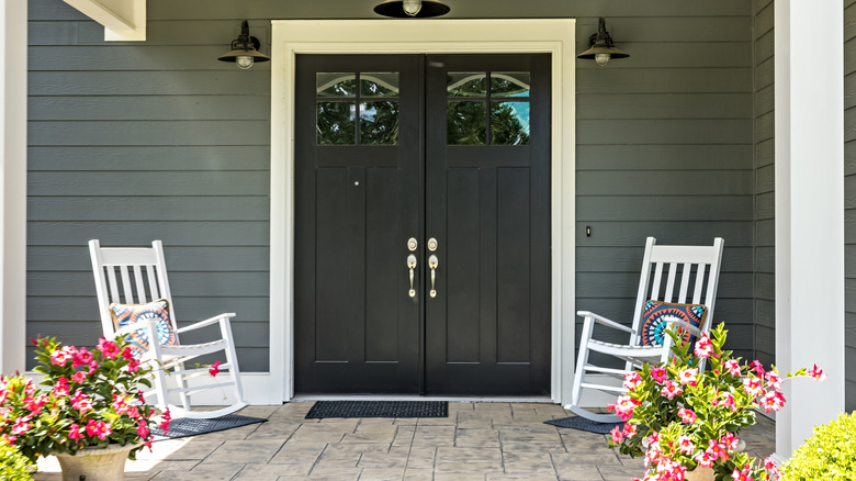 The front porch of a home with two white rocking chairs and flower pots with pink flowers