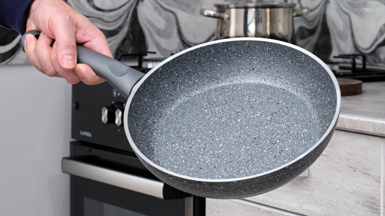 A hand holding a non-stick frying pan in a modern kitchen.