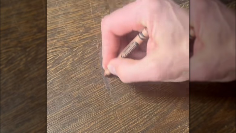 Hand rubbing a brown crayon on a hardwood floor stain