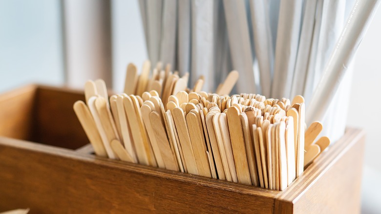 A wooden organizer holding straws and sticks