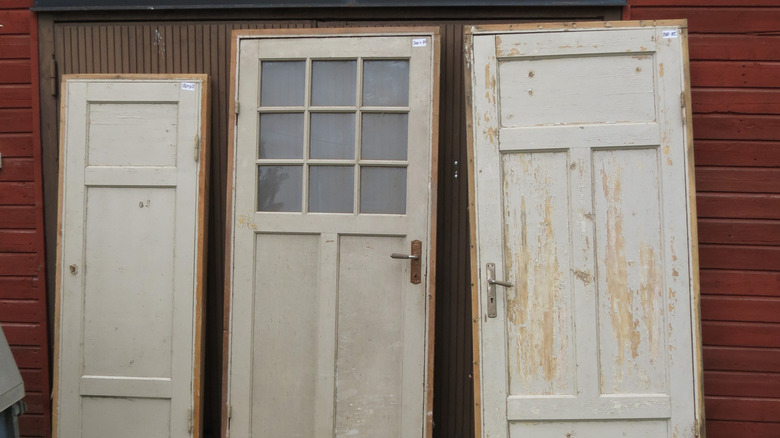 Three old wooden doors leaning against the wall of a building