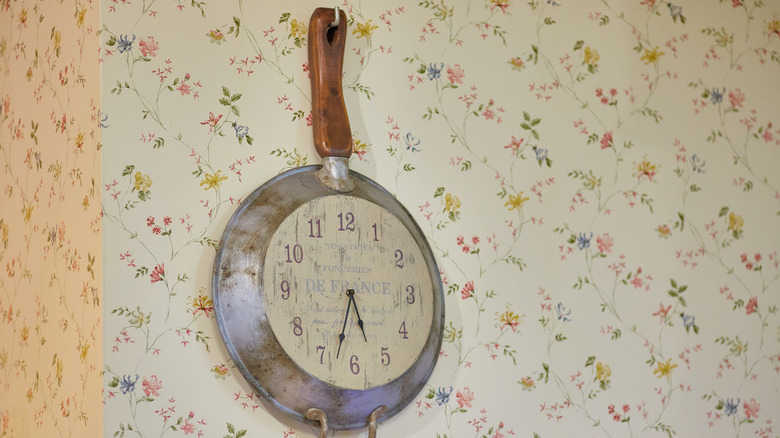 Analog clock made from frying pan hanging on wall hook