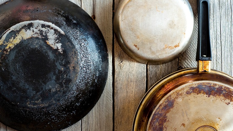 Three worn frying pans hanging on wooden wall