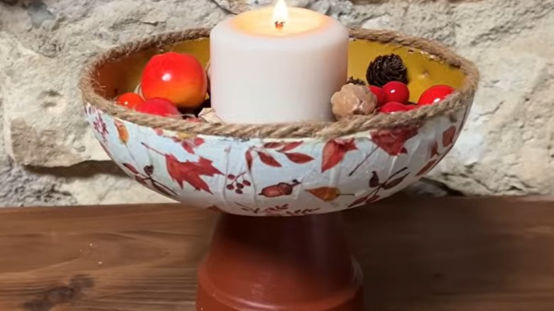 A candle and decorative faux fruit sit in a container made from an old frying pan.