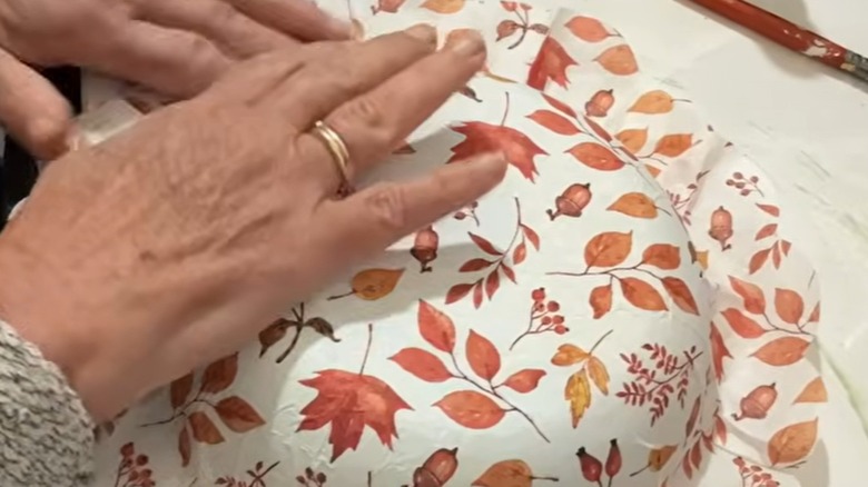 Light-skinned hands smooth a decoupage napkin over a pan covered in Mod Podge.