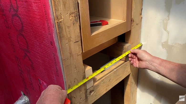 A person measuring the framing of a bathroom hidden cabinet under construction