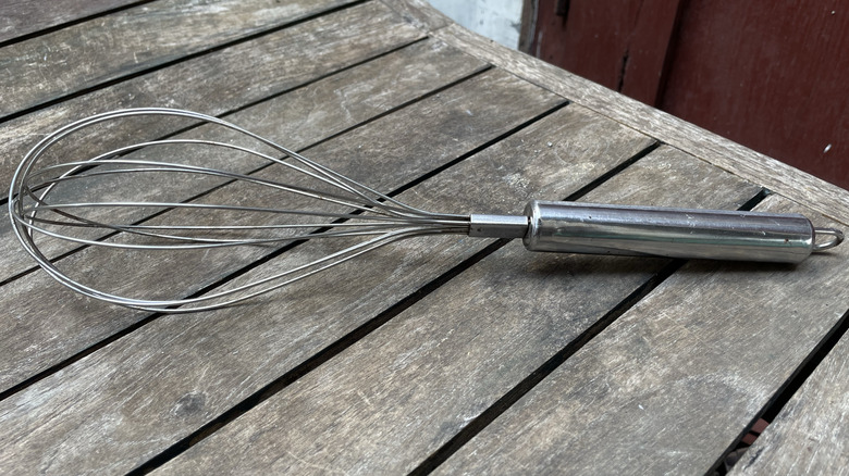 A whisk sitting outdoors on some weathered wood.