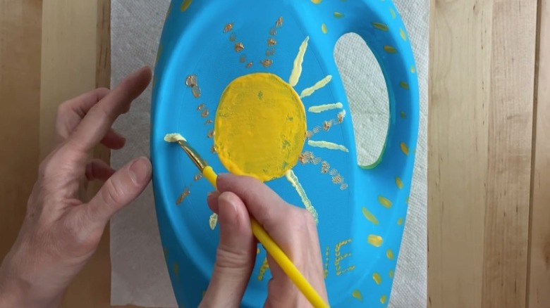 Person painting yellow designs on blue detergent bottle