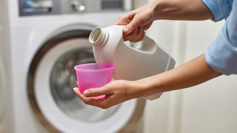 Person pouring a detergent bottle in front of a washing machine