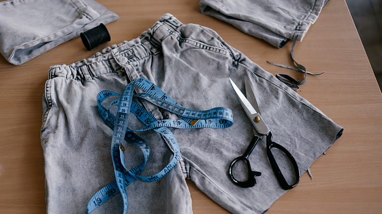 Scissors and measuring tape on top of a cut-up pair of jeans