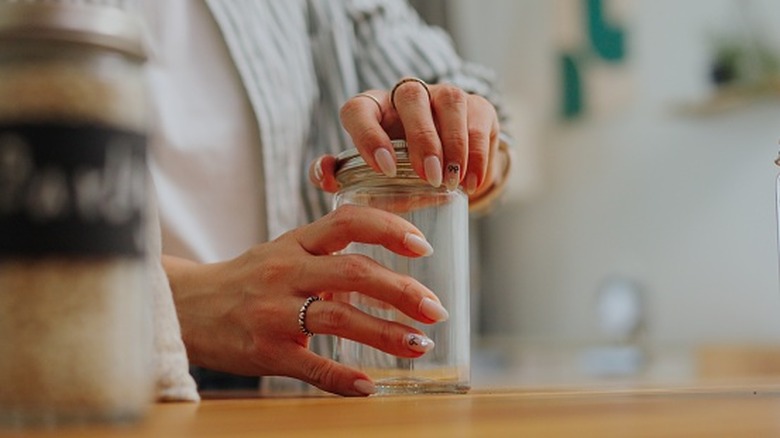 A woman's manicured hands open an empty glass pickle jar