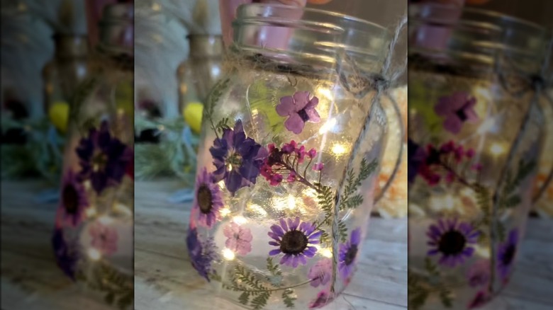 A glass jar covered in pressed flowers and has fairy lights inside