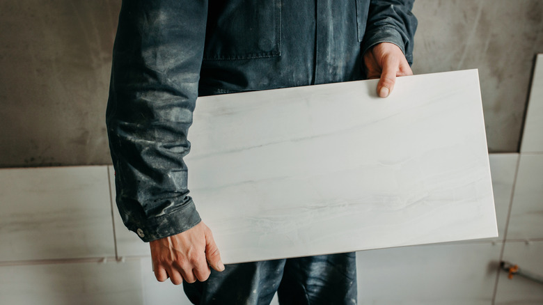 A person holding a large white tile