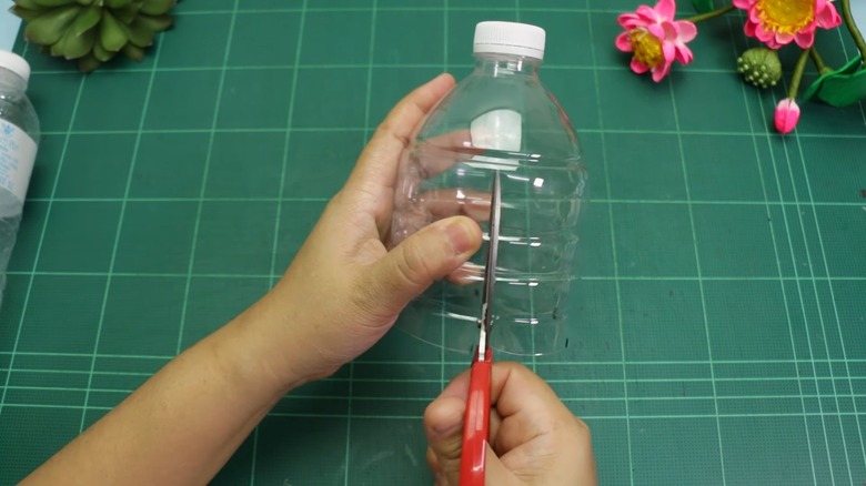 Hands holding a half-cut plastic bottle and snipping it vertically