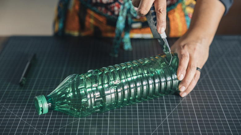 Person cutting a plastic bottle with a utility knife.