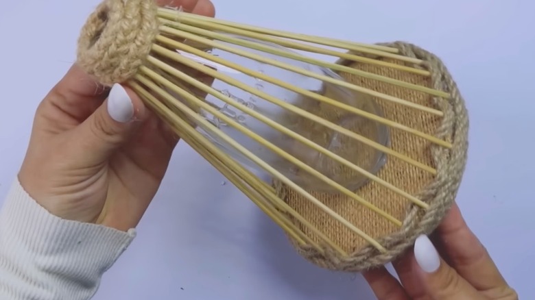 Bamboo skewers and a burlap base upgrade a glass bottle into a decorative vase.