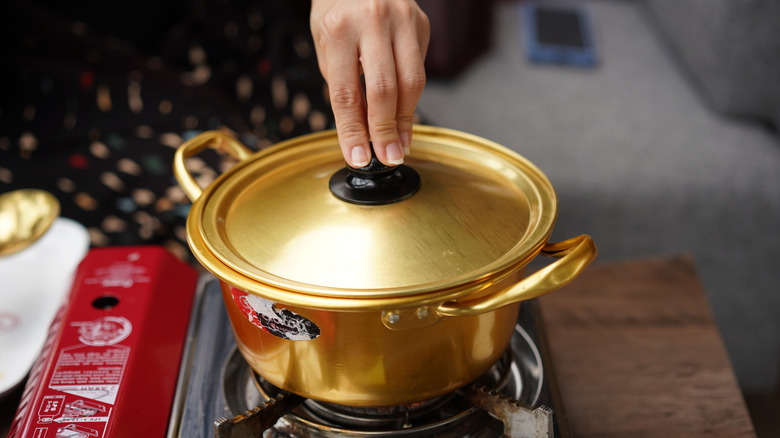 hand touching gold metal pot with lid