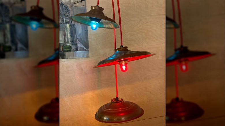 Three pendant mood lamps made from metal pot lids hang from red cords.