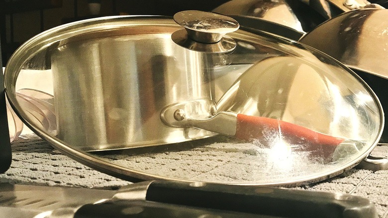 Close-up of a pot lid drying with a saucepan and other cookware seen in the background