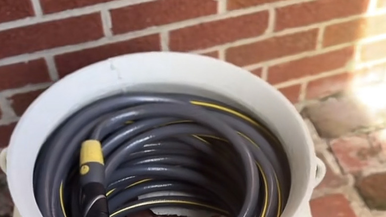 A black garden hose coiled inside a painted metal plant pot with an open base.