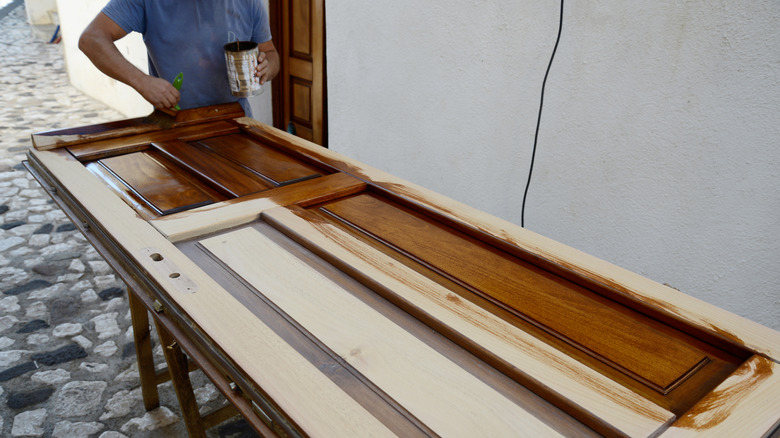 Man painting a door propped on sawhorses with a dark stain
