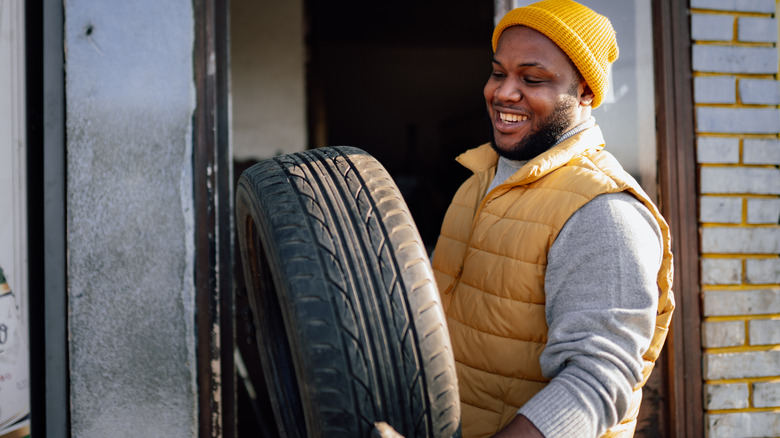 A smiling man carrying an old tire